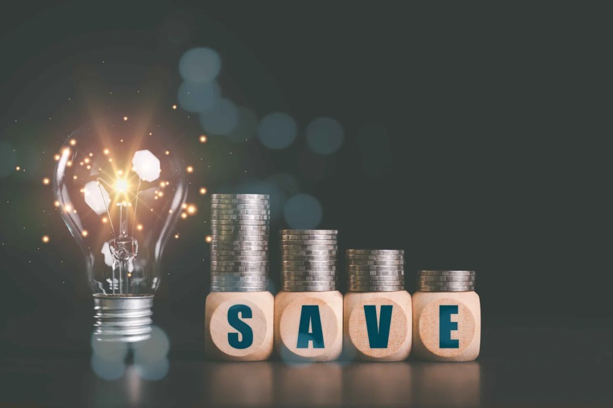 Glowing light bulb and wooden blocks spelling "SAVE" with coins.